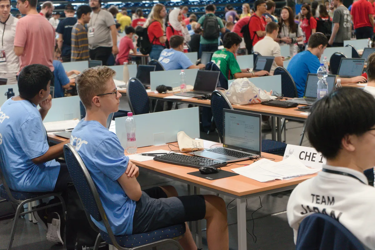 351 Talente aus 87 Ländern massen sich an der Informatik-Olympiade in Szeged (Ungarn). Viele junge Leute sitzen in einer Halle vor ihren Notebooks.